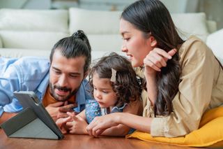 Parents and young girl work at tablet computer.