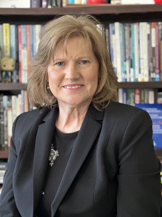 A headshot of Barbara Malkas. She is dressed formally and standing in front of a bookshelf.